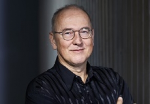 Ian Munro, a man wearing glasses and a black buttonup shirt smiling with his mouth closed