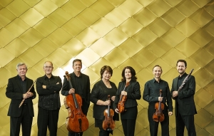 7 members of the Australia Ensemble standing in front of a gold cladded wall holding their instruments