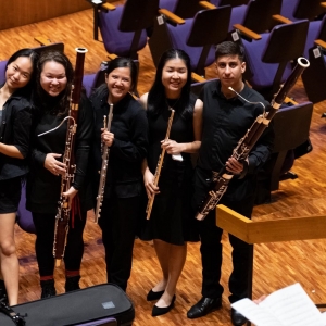 Five university students wearing black standing in an auditorium holding their woodwind instruments. They smile at the camera.