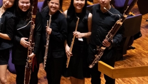 Five university students wearing black standing in an auditorium holding their woodwind instruments. They smile at the camera.