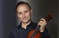 Dene Olding, wearing a black collared shirt and holding a violin