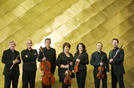 7 members of the Australia Ensemble standing in front of a gold cladded wall holding their instruments